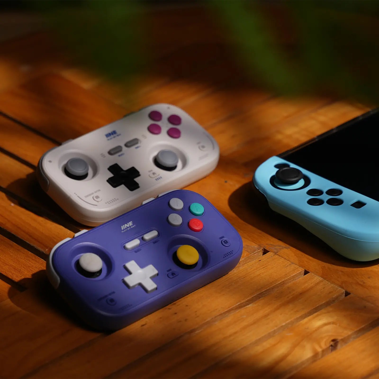 White and purple IINE Retro Pocket controllers arranged in a warm gaming setup